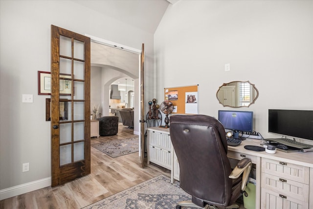 office area featuring arched walkways, baseboards, vaulted ceiling, light wood-style floors, and french doors