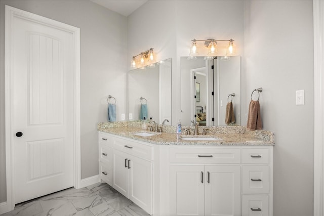 bathroom featuring double vanity, marble finish floor, baseboards, and a sink