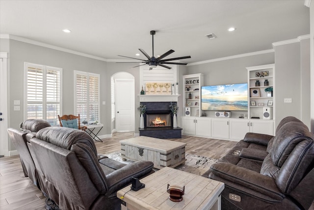 living room featuring light wood-style flooring, visible vents, ornamental molding, and a lit fireplace