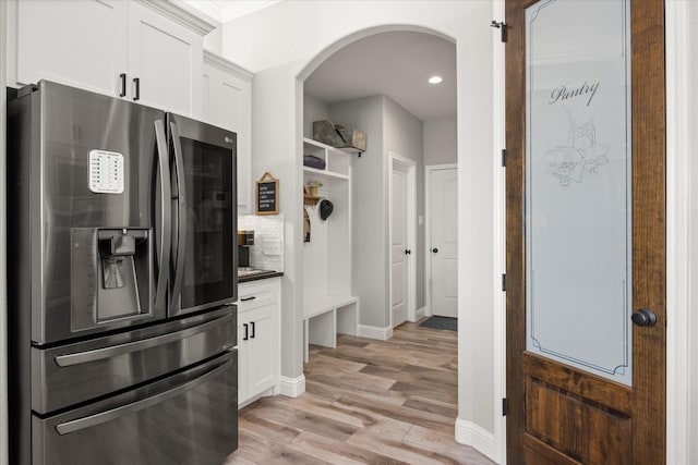 kitchen featuring stainless steel refrigerator with ice dispenser, dark countertops, backsplash, white cabinets, and light wood-type flooring