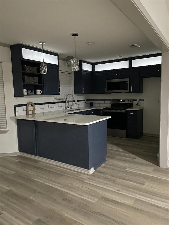 kitchen with sink, appliances with stainless steel finishes, decorative light fixtures, kitchen peninsula, and light wood-type flooring