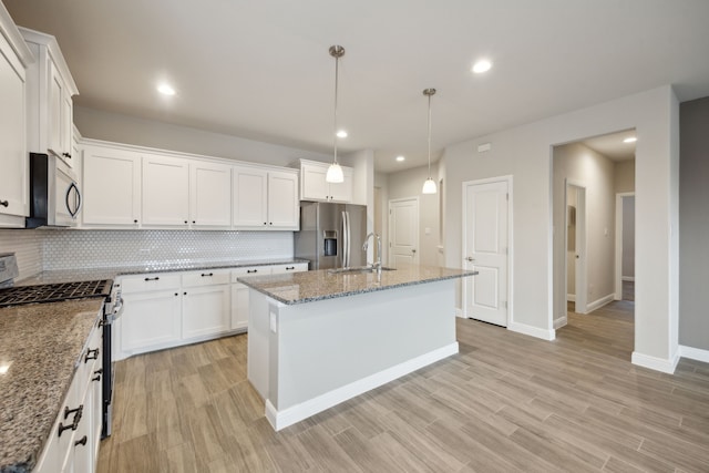 kitchen with pendant lighting, sink, appliances with stainless steel finishes, a kitchen island with sink, and white cabinetry