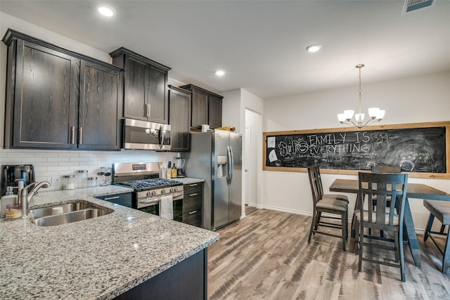 kitchen with appliances with stainless steel finishes, decorative light fixtures, tasteful backsplash, sink, and light stone counters
