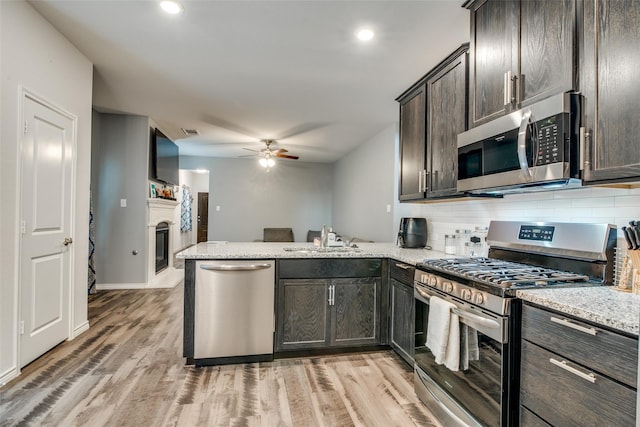 kitchen with sink, stainless steel appliances, dark brown cabinetry, light stone countertops, and kitchen peninsula