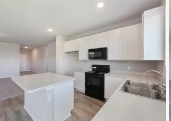 kitchen featuring sink, white cabinetry, black appliances, a kitchen island, and light wood-type flooring