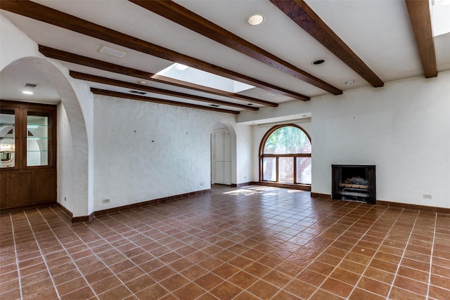 unfurnished living room featuring beamed ceiling and dark tile patterned flooring