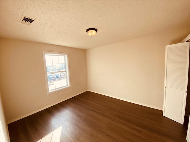 empty room with dark hardwood / wood-style floors and a textured ceiling