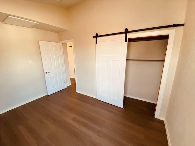 unfurnished bedroom with a closet, dark hardwood / wood-style floors, and a barn door