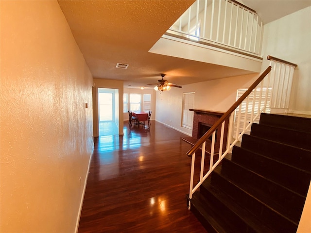 stairway with hardwood / wood-style flooring, a textured ceiling, ceiling fan, and a fireplace