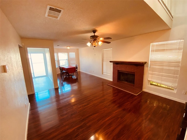 unfurnished living room with ceiling fan, a brick fireplace, dark hardwood / wood-style floors, and a textured ceiling