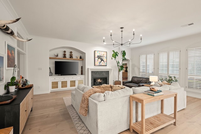 living room with a notable chandelier, crown molding, built in features, and light wood-type flooring