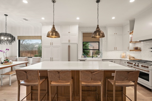 kitchen featuring a kitchen island, pendant lighting, high quality appliances, white cabinetry, and crown molding