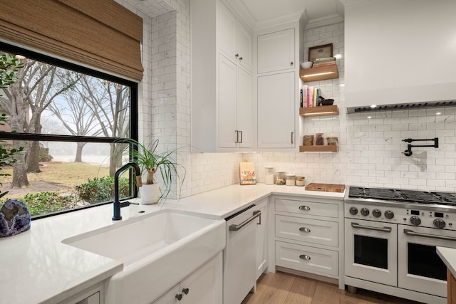 kitchen featuring sink, range with two ovens, white cabinetry, crown molding, and decorative backsplash