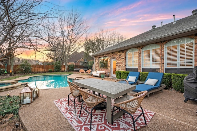 pool at dusk featuring an in ground hot tub and a patio area