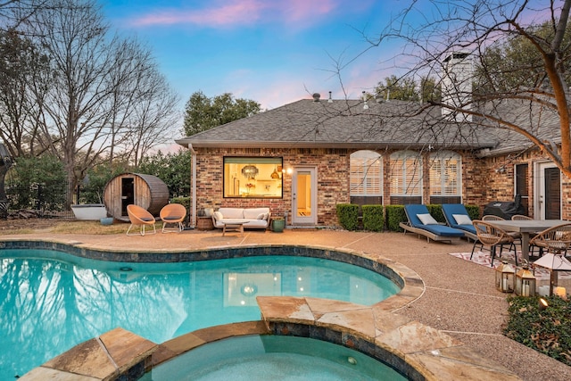 pool at dusk with a storage shed, an outdoor living space, a patio area, and an in ground hot tub