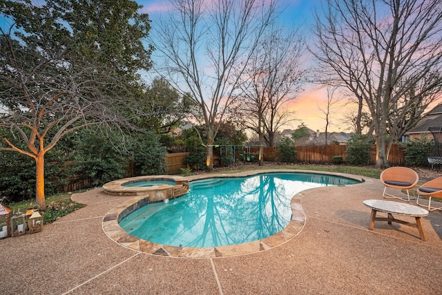 pool at dusk featuring an in ground hot tub and a patio area