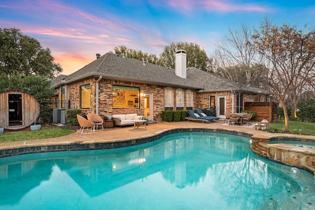 pool at dusk featuring an in ground hot tub, outdoor lounge area, central air condition unit, and a patio area