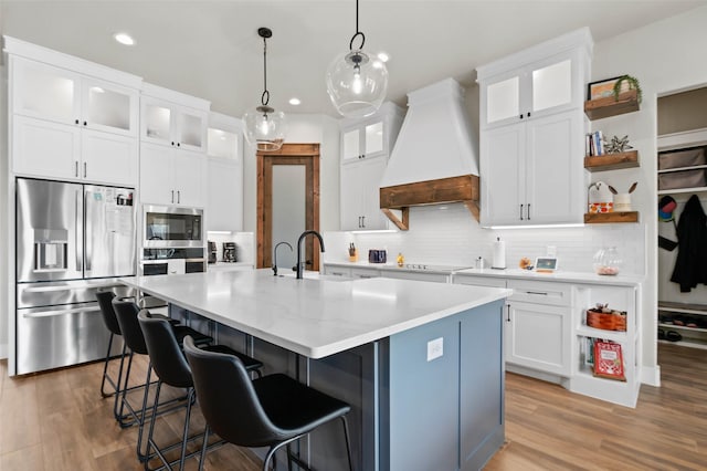 kitchen with a center island with sink, appliances with stainless steel finishes, custom exhaust hood, and white cabinets