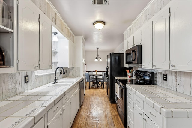 kitchen featuring visible vents, tile counters, decorative backsplash, black appliances, and a sink