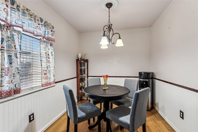 dining space featuring light wood-type flooring, a wealth of natural light, a notable chandelier, and wainscoting