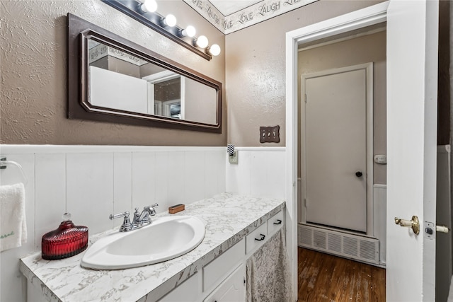 bathroom featuring a textured wall, a wainscoted wall, wood finished floors, visible vents, and vanity