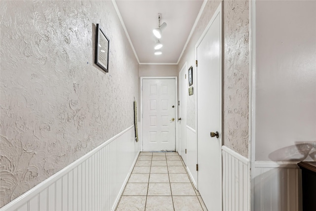 corridor with light tile patterned floors, ornamental molding, and wainscoting