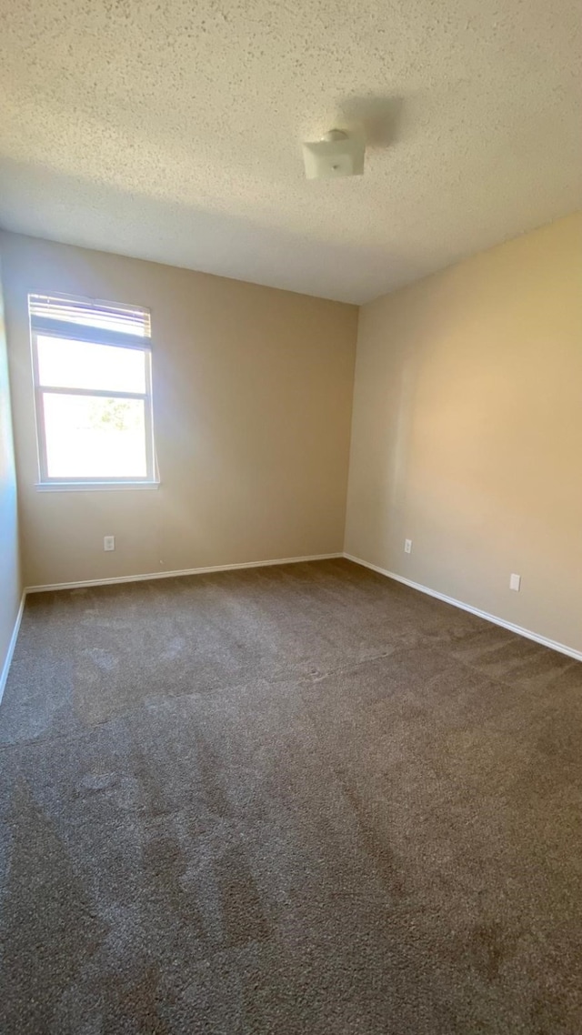 spare room featuring a textured ceiling, dark carpet, and baseboards