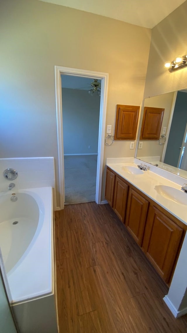 full bathroom with a sink, a bath, and wood finished floors