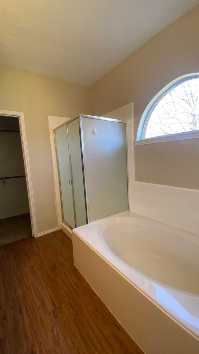 full bathroom with a stall shower, a bath, and wood finished floors