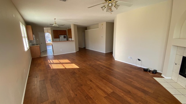 unfurnished living room featuring baseboards, a fireplace, a ceiling fan, and wood finished floors