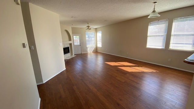 unfurnished living room with baseboards, a ceiling fan, a tile fireplace, dark wood-style flooring, and a textured ceiling