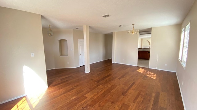 empty room featuring baseboards, visible vents, an inviting chandelier, and wood finished floors