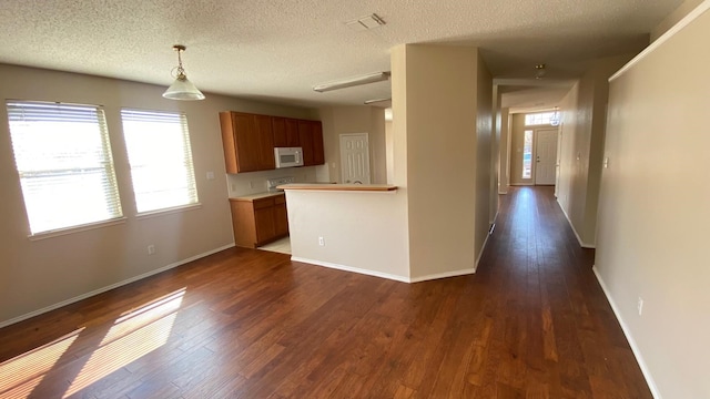 kitchen featuring white microwave, baseboards, dark wood-style floors, and brown cabinetry