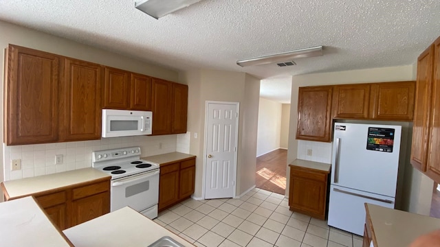 kitchen featuring white appliances, visible vents, brown cabinets, and light countertops