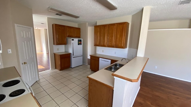 kitchen with visible vents, brown cabinetry, a sink, white appliances, and a peninsula