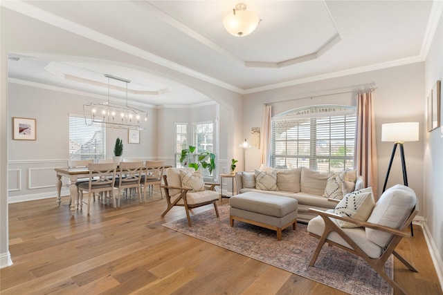 living room with crown molding, a tray ceiling, a wealth of natural light, and light hardwood / wood-style floors