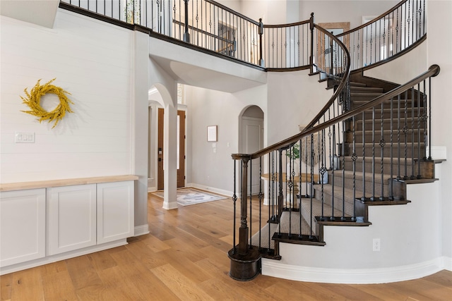 stairway with baseboards, a high ceiling, arched walkways, and wood finished floors