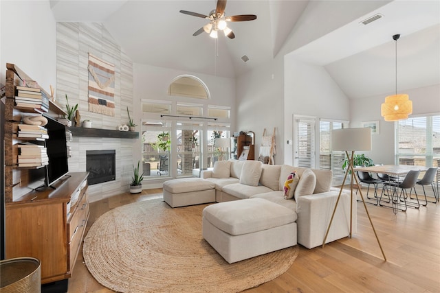 living room with high vaulted ceiling, a tile fireplace, ceiling fan, and light wood-type flooring