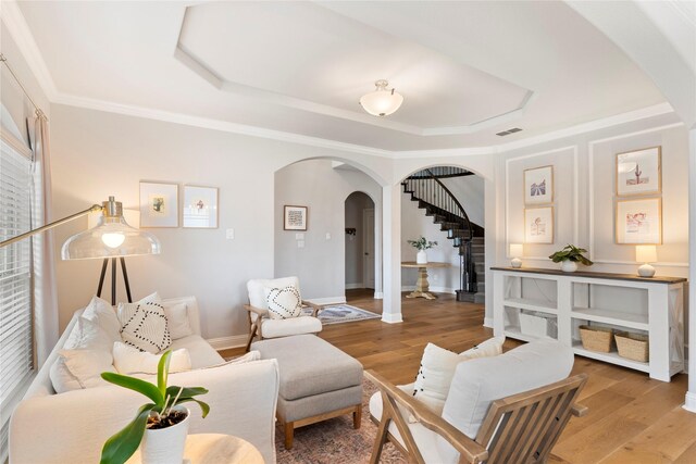 living room with arched walkways, crown molding, visible vents, wood finished floors, and stairs