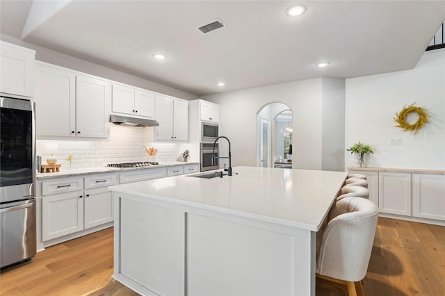 kitchen with sink, appliances with stainless steel finishes, white cabinetry, a center island with sink, and light wood-type flooring