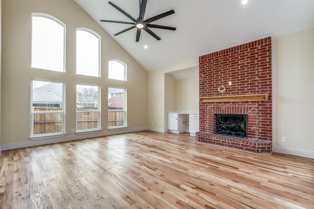 unfurnished living room with ceiling fan, high vaulted ceiling, a fireplace, and light hardwood / wood-style flooring