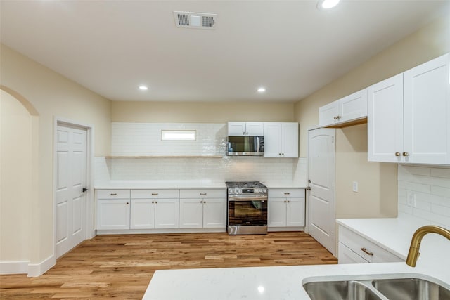 kitchen with tasteful backsplash, light hardwood / wood-style floors, white cabinets, and appliances with stainless steel finishes