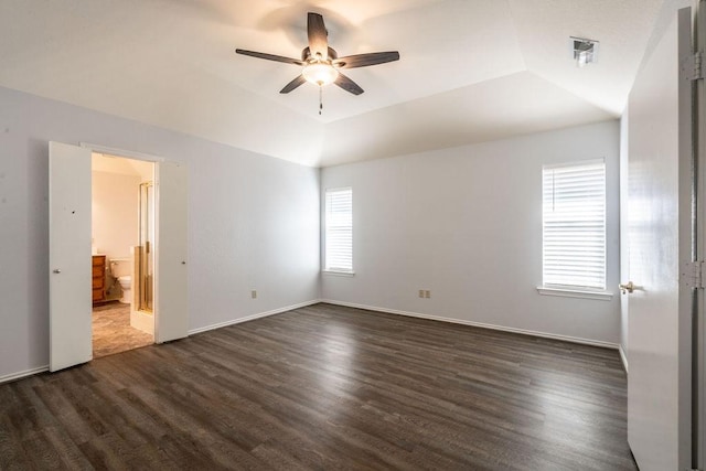 unfurnished bedroom featuring dark wood-type flooring, ensuite bath, ceiling fan, vaulted ceiling, and a tray ceiling