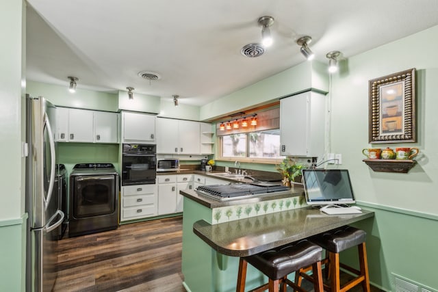 kitchen with appliances with stainless steel finishes, a breakfast bar area, white cabinets, kitchen peninsula, and washing machine and dryer