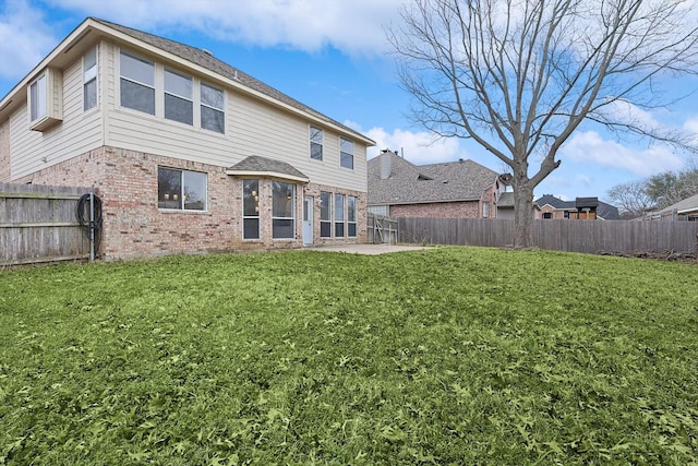 rear view of house with brick siding, a yard, and a fenced backyard