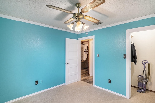 unfurnished bedroom featuring crown molding, a walk in closet, carpet, baseboards, and a textured ceiling