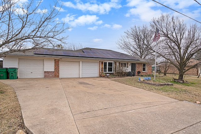 ranch-style home with an attached garage, roof mounted solar panels, concrete driveway, and brick siding