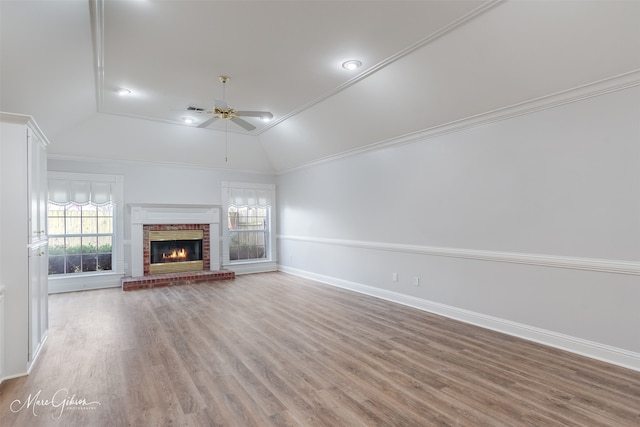 unfurnished living room with vaulted ceiling, ornamental molding, ceiling fan, a brick fireplace, and light wood-type flooring