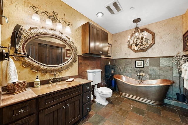 bathroom featuring toilet, tile walls, vanity, a bathing tub, and a notable chandelier