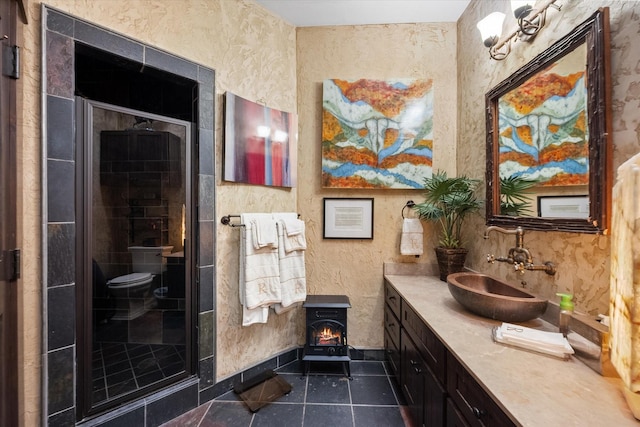 bathroom featuring toilet, a shower with shower door, a wood stove, vanity, and tile patterned flooring